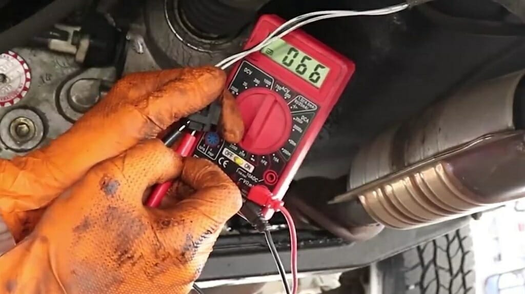 A person with orange gloves testing the signal wire with multimeter at 066v reading