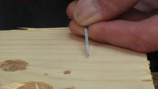 A person using an awl to hammer a hole on a wood