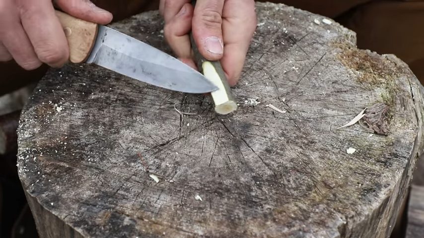 A person using knife to drill a hole on a piece of wood stick