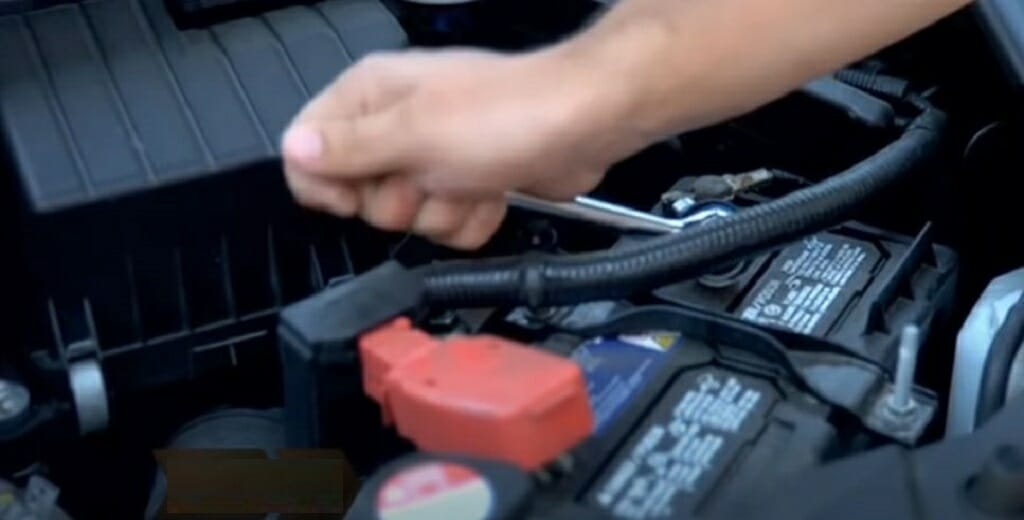A person disconnecting a battery using a wrench