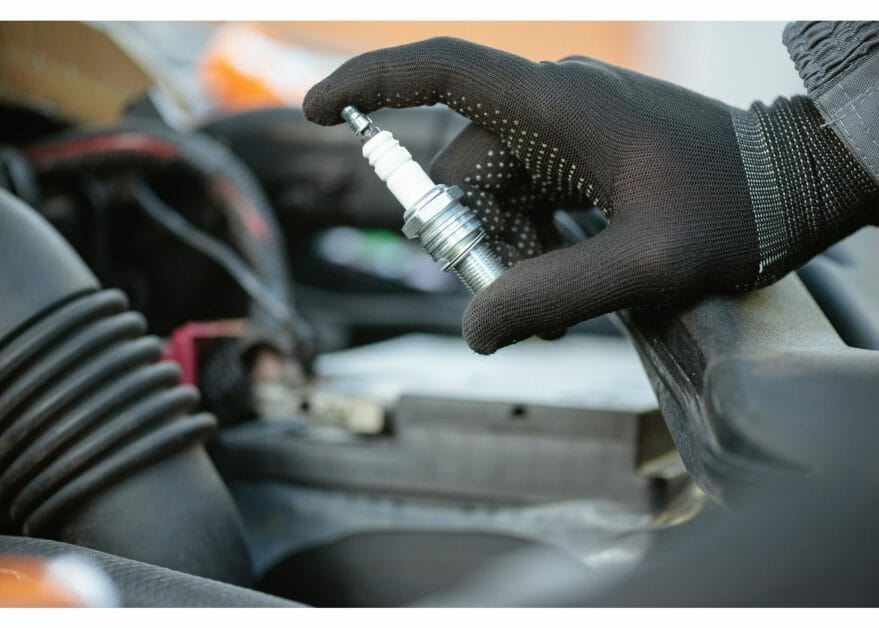 mechanic in black gloves holding spark plug