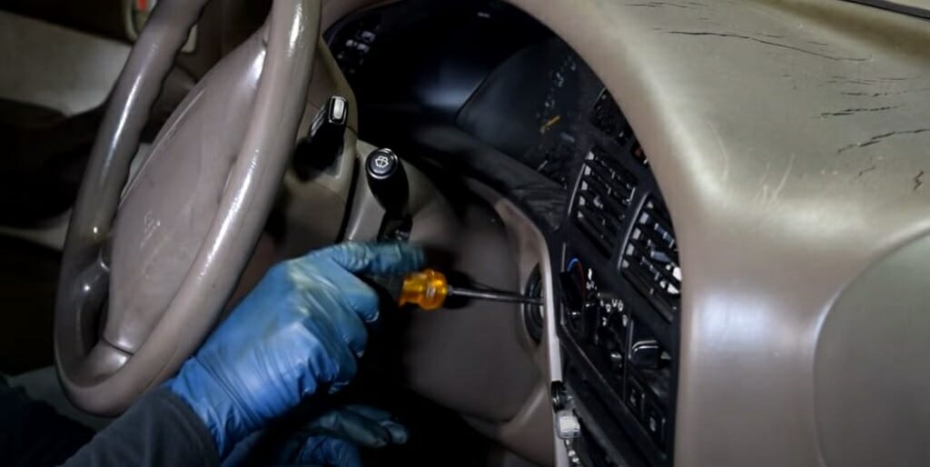 mechanic in blue gloves inserting screwdriver at the keyhole