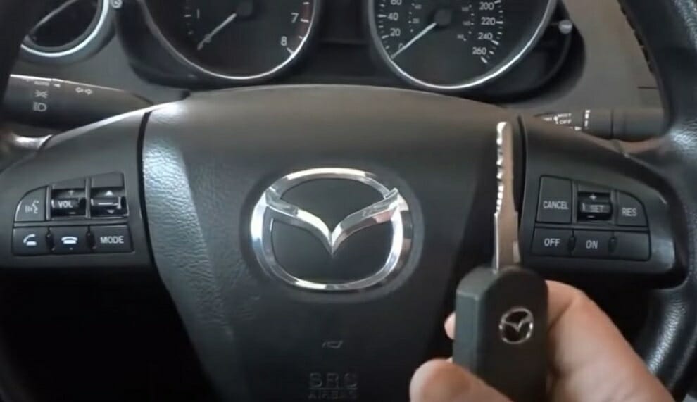 hand holding a car key in front of the steering wheel