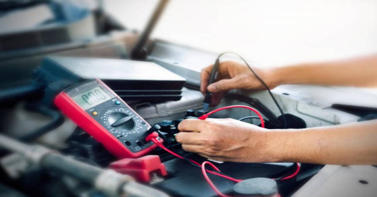 A man using a multimeter to check the battery of a car and detect any potential battery drain