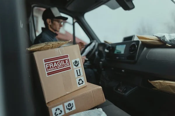 a delivery car with the driver along with a box that has fragile sticker