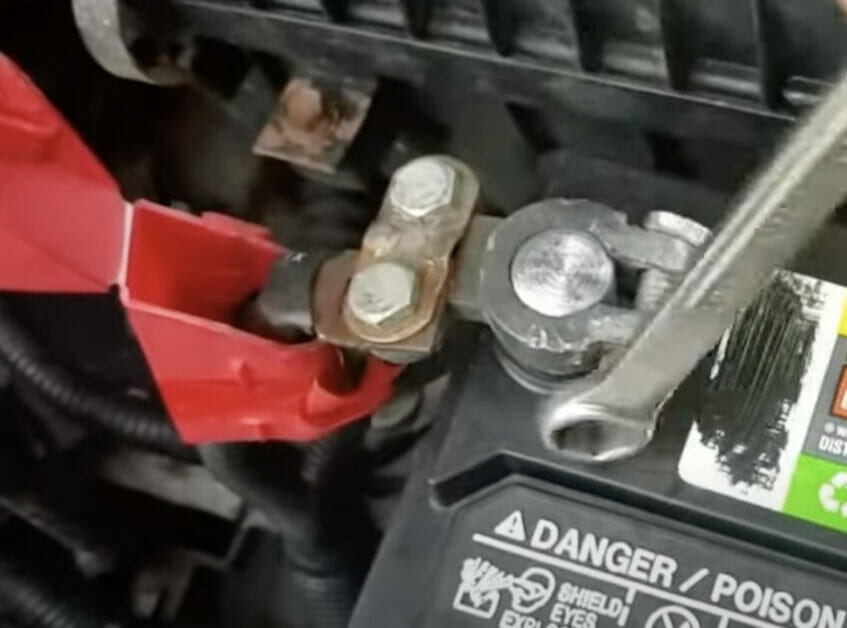 A person connecting the positive (red) terminal of a car battery
