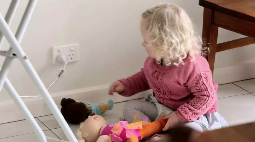a baby girl playing with her dolls beside an outlet wall
