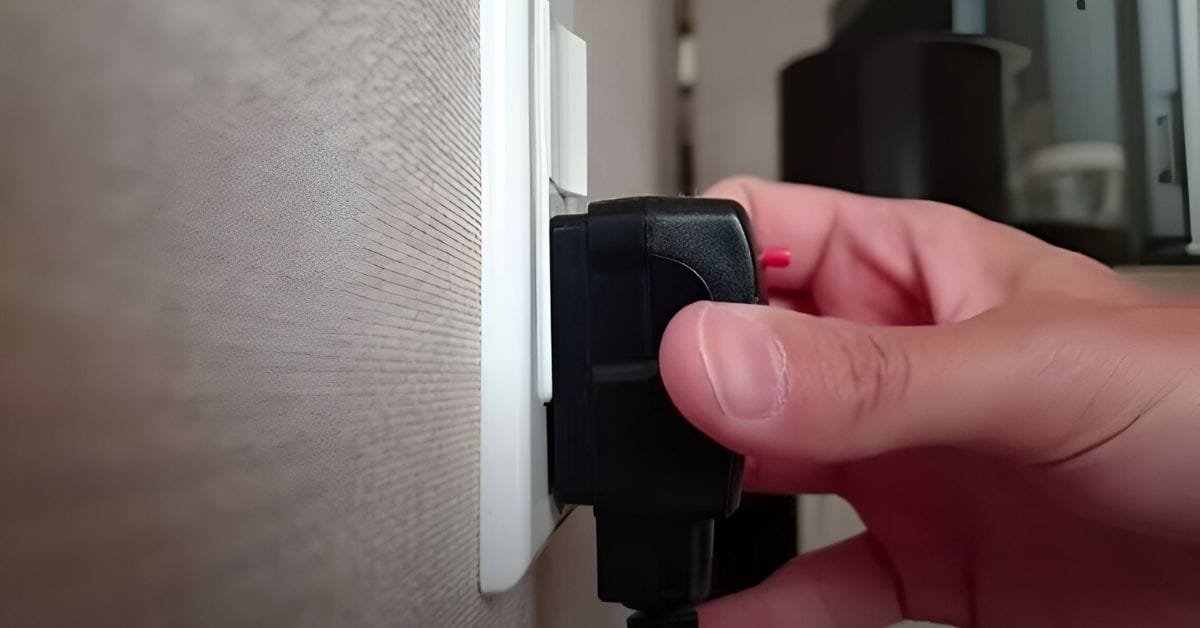 A closer image of a hand plugging a wire into the wall outlet