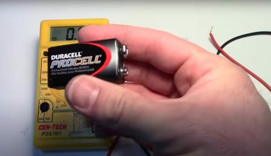 a hand holding a duracell procell battery with multimeter in the background