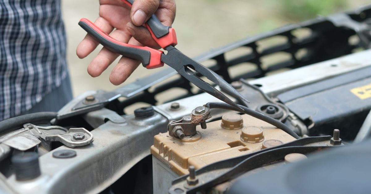 A person holding pliers to a car battery.
