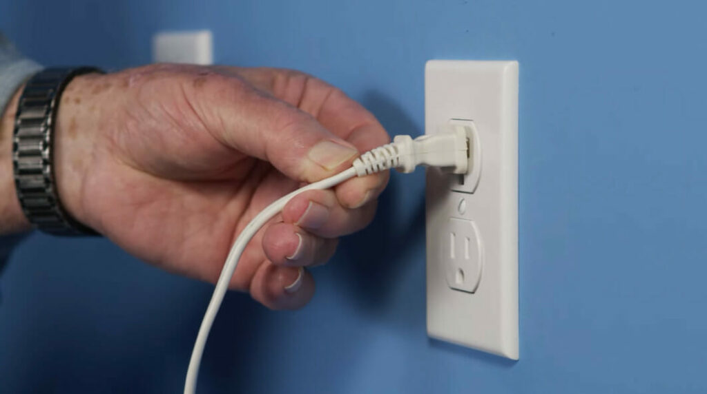 a man's hand holding a loose electrical plug into the outlet