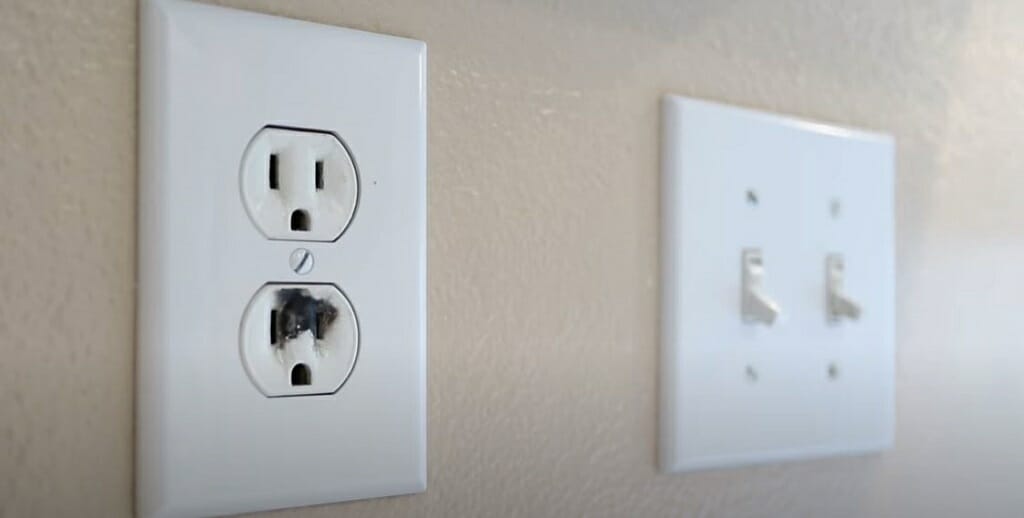 burnt prong outlet beside a switch on the wall