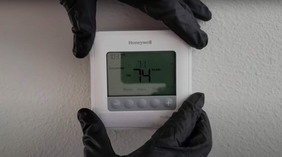 honeywell thermostat held by a hand with black gloves