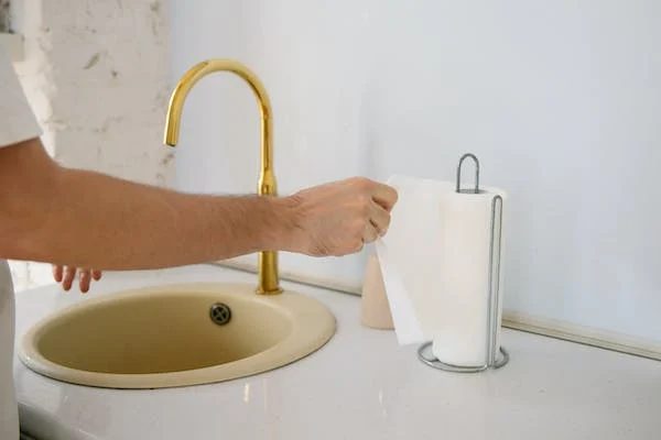 man getting a paper towel after washing on the sink