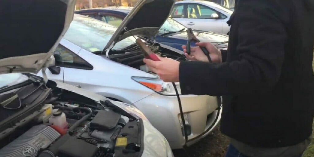 man holding the battery clip with an open car hood in front of him
