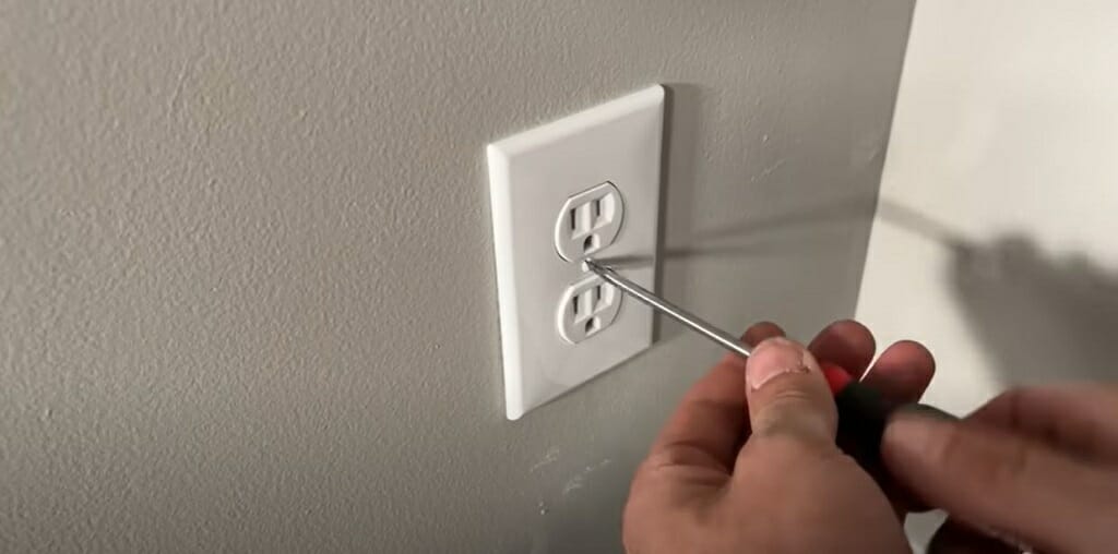 man opening the cover of the wall outlet using a screwdriver