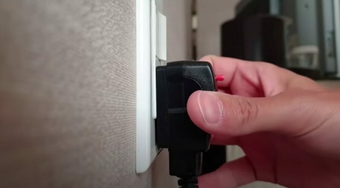 man's hand plugging wire into a wall outlet