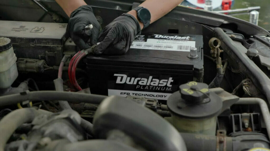 mechanic with black gloves connecting a duralast battery on the car hood