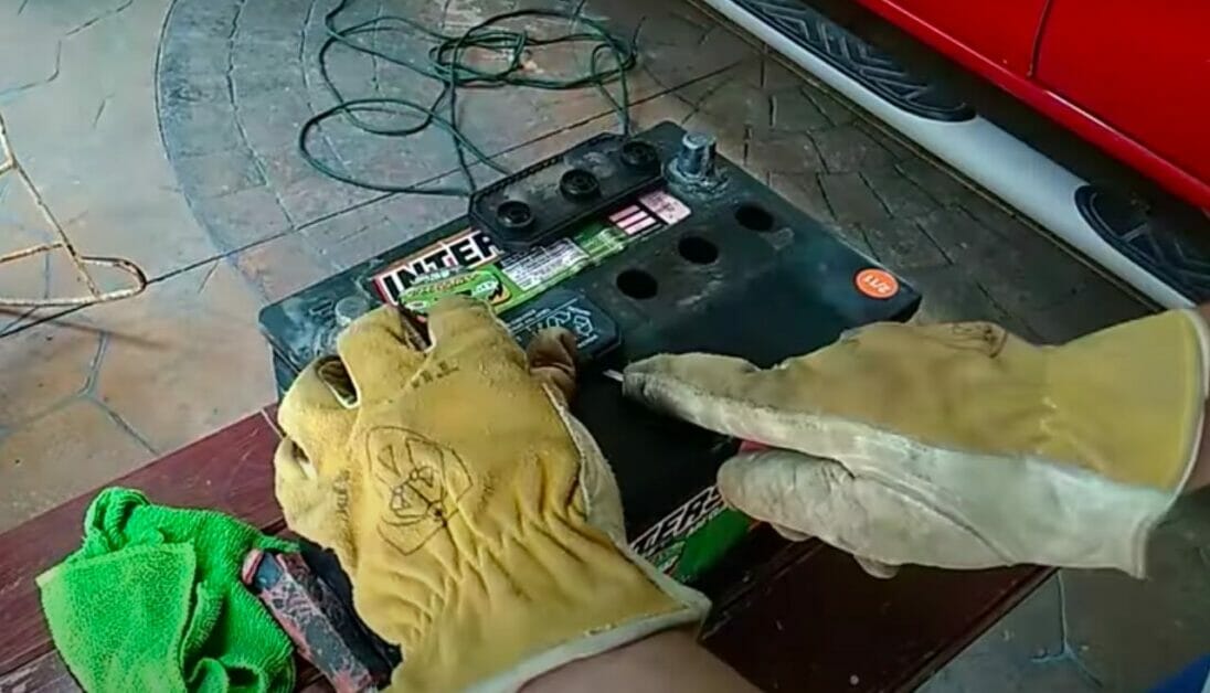 mechanic with yellow torn gloves opening the car battery for restoration