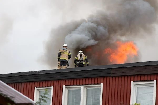 two firemen at the top of a home's roof working to stop the fire