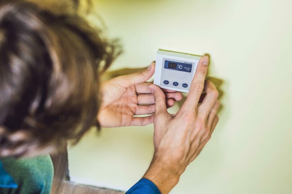 man installing a thermostat on a home