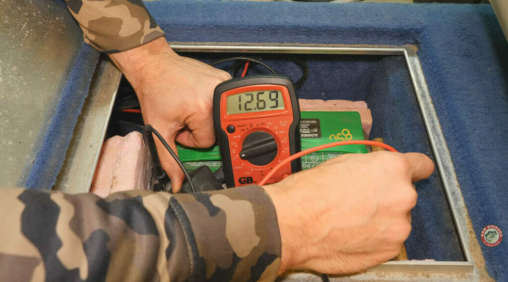 man with a camouflage long sleeve shirt testing the batter with a multimeter