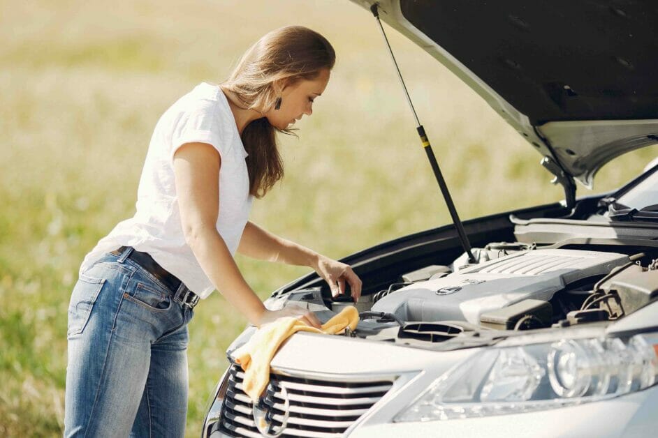 woman in white tee and jeans checking on her car engine