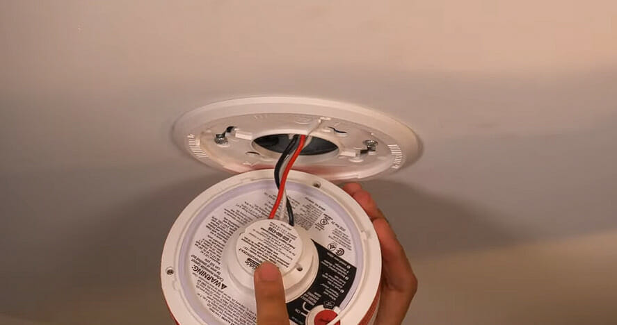 man flipping the other side for a hard-wired smoke detector