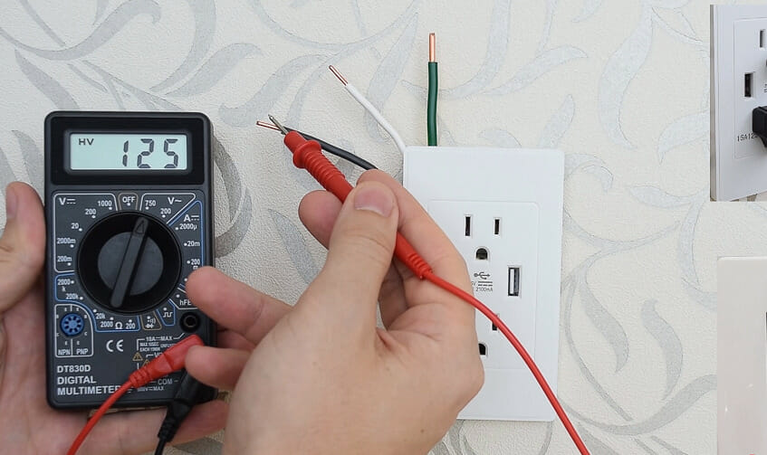 man holding a multimeter and testing the wires on an outlet