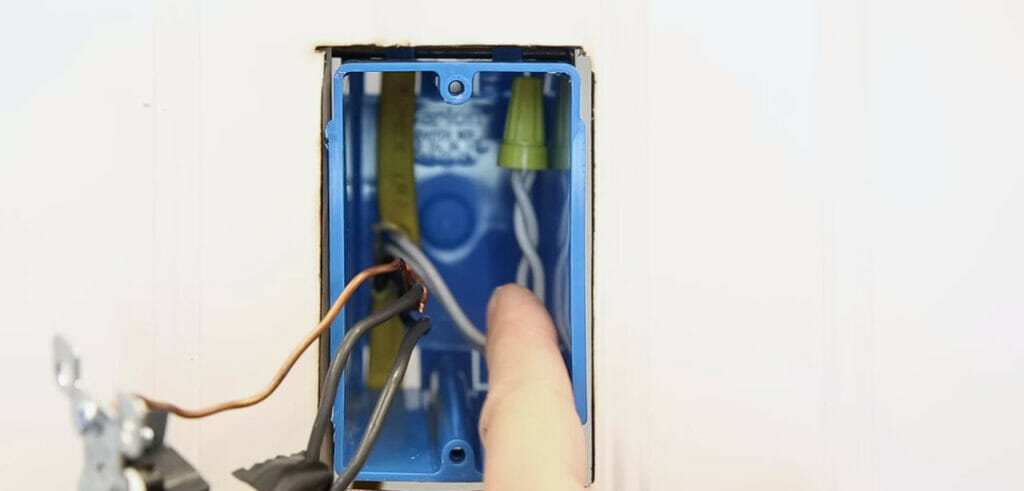 man pointing out at a gray wire in an undone blue electrical box