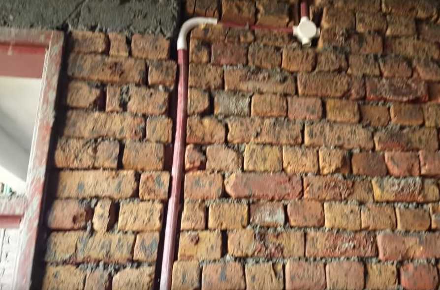 A brick wall with a concealed red pipe
