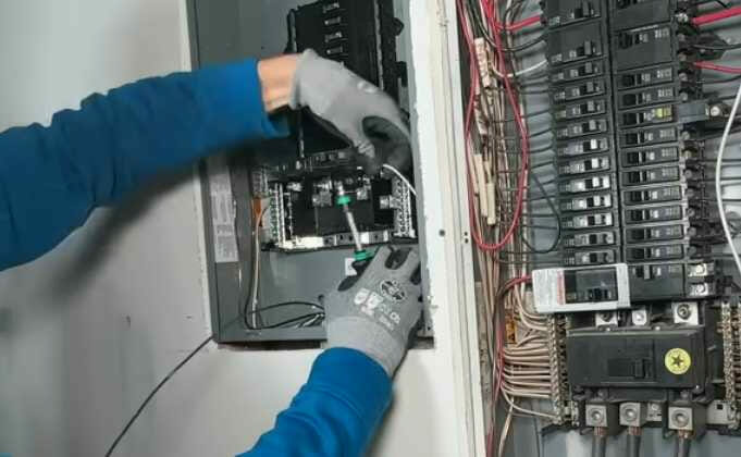 A man blue jacket and gray gloves is working on an electrical panel