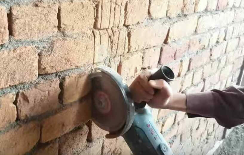 A man demonstrates wire hiding techniques on a brick wall using a grinder