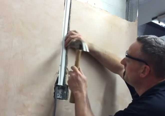 A man is working on a wall with a hammer to hide wires