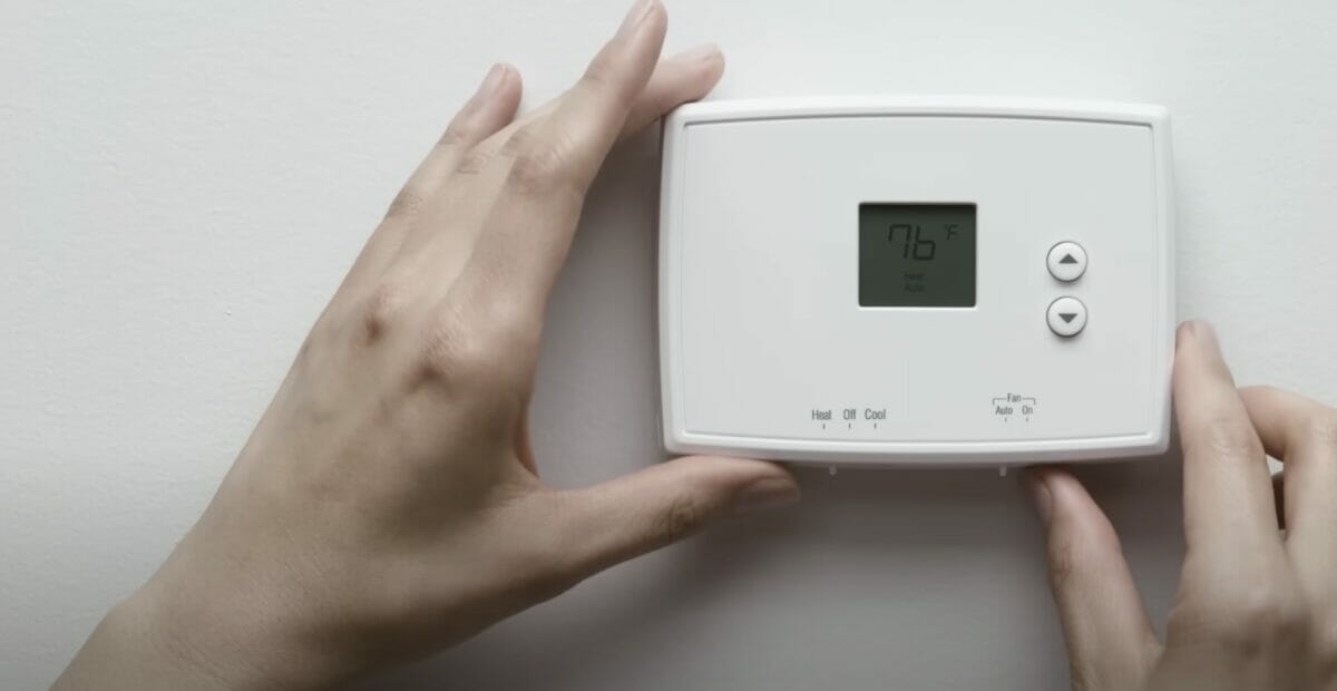 A person holding a digital thermostat on a wall