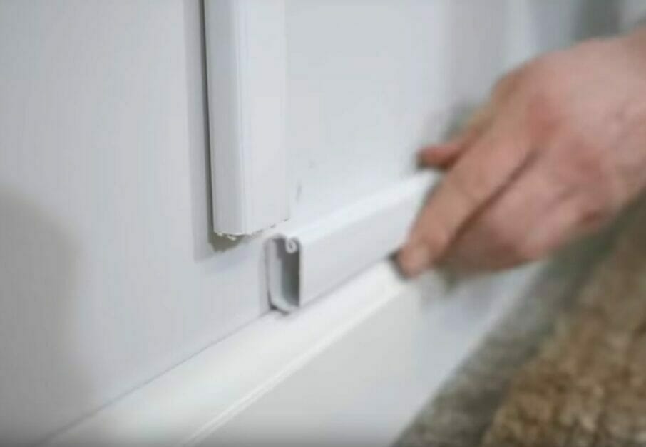 A person installing a white conduit on the wall to hide wire