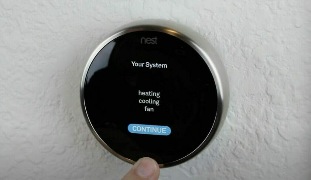 A person is pointing at a nest smart thermostat