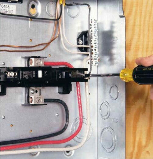 A person is using a screwdriver to connect wires to an electrical panel