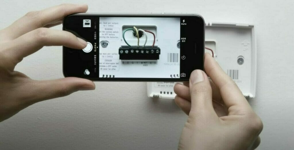 A person photographing a smart thermostat
