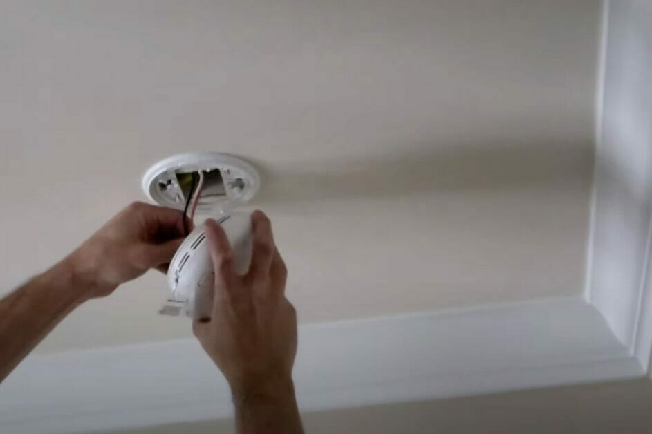 A man installing a hardwired smoke detector in a ceiling.