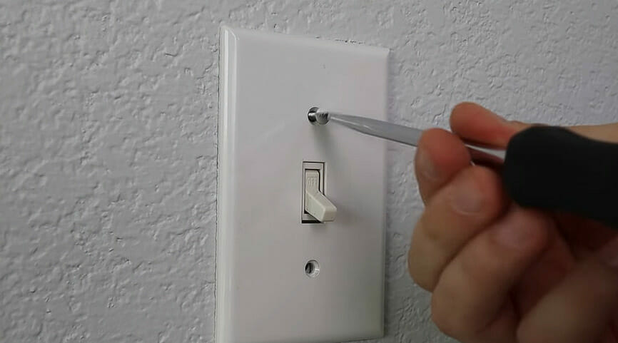 A man unscrewing the white outlet switch on a white wall