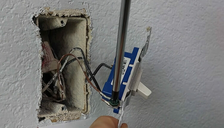 A man disconnecting wire on a single pole light switch using screw