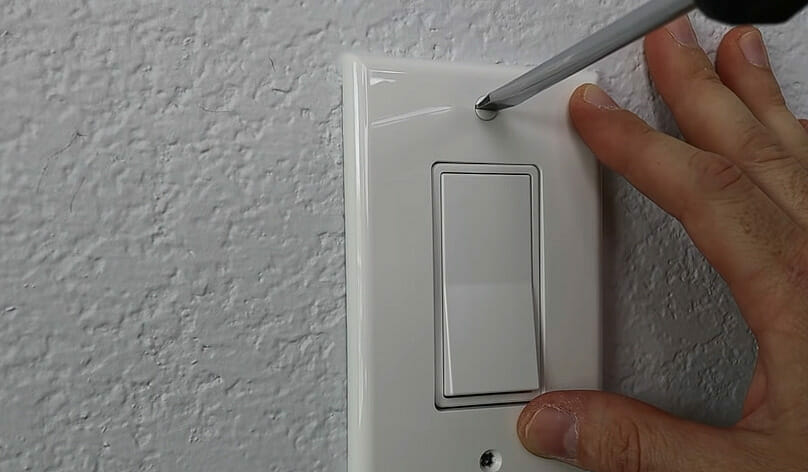 A person screwing the switch into place and attach the cover plate