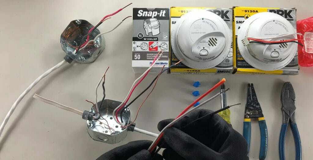 A person is working with wires on a table to wire a smoke detector
