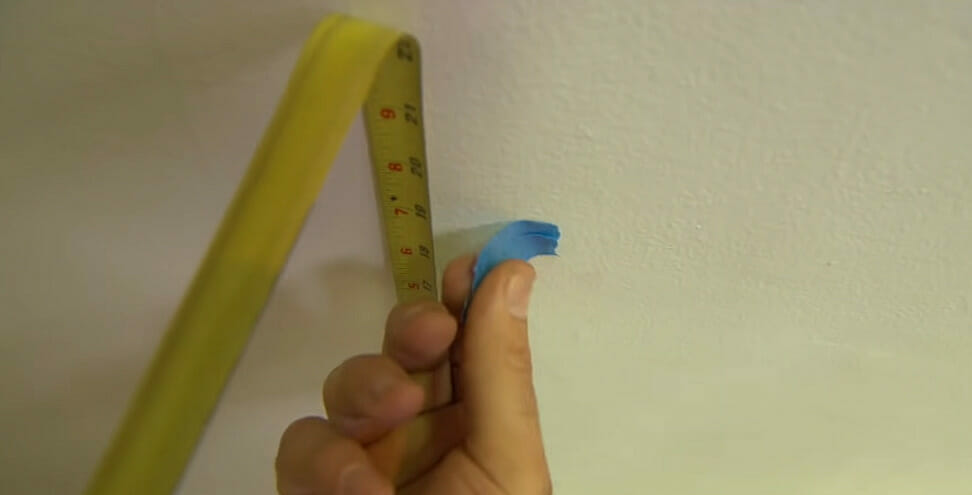 A person measuring and marking the wall for wiring a smoke detector