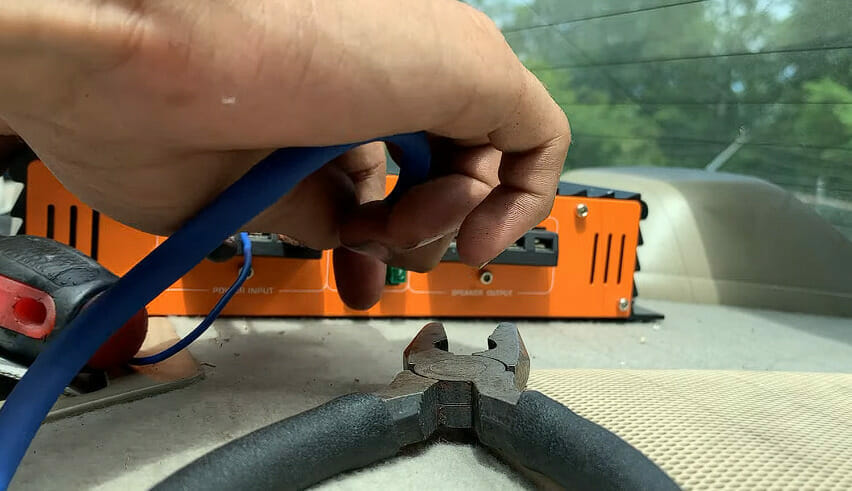 A person using a plier to connect the power wire into the speaker's receiver