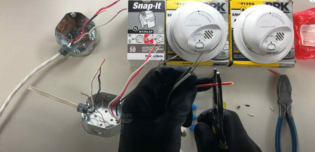A man with black gloves stripping wires for smoke detector