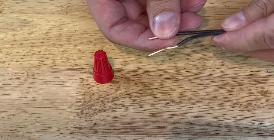 A person is using red wire nuts to cap a black wire