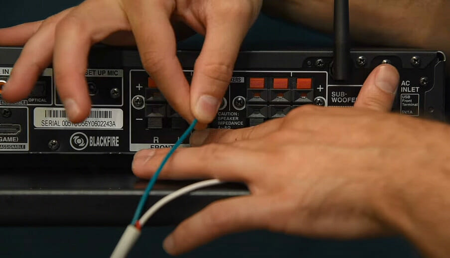 A person inserting speaker wires at the back of the speaker receiver box