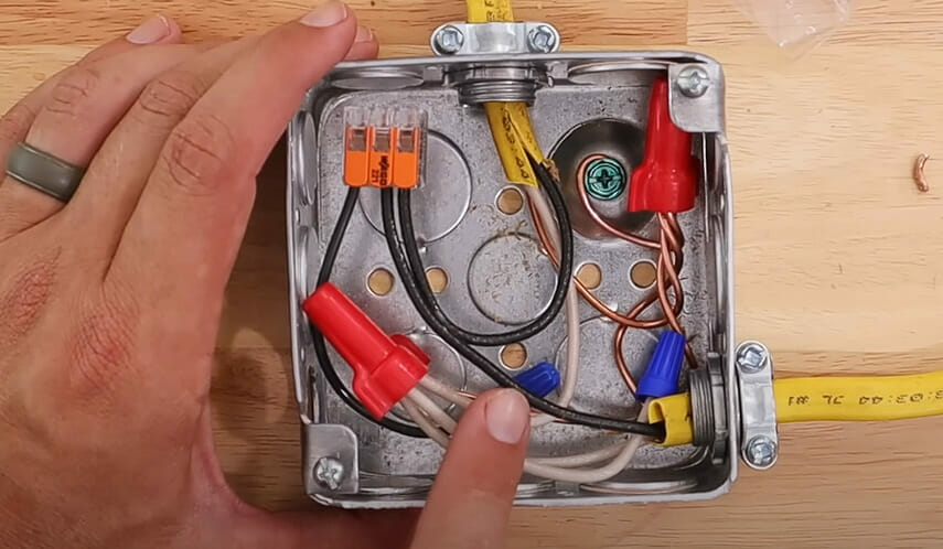 A person is connecting 14 gauge wires with a red wire nut in a metal box